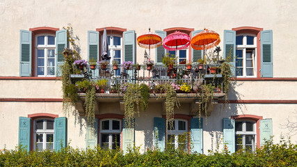A charming balcony features bright umbrellas and lush greenery, showcasing floral arrangements in a welcoming residential setting
