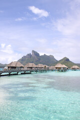 Overwater bungalows in Bora Bora with Mount Otemanu view, turquoise lagoon, calm waters, and partly cloudy tropical sky – French Polynesia island paradise