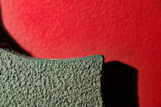 Closeup detail of showcasing the rough, textured edge of a green material against a stark red background. Textures, colors, and shadows create an abstract and engaging composition. Textured background