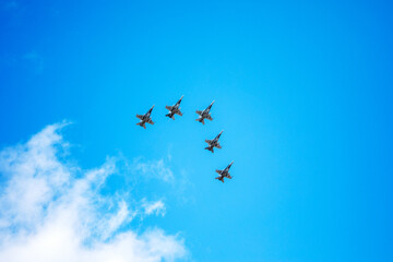 A fleet of five military fighter aircraft flying in tight formation under a vivid blue sky with...