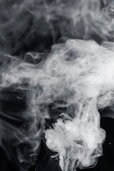 Closeup view of swirling smoke, creating an ethereal and abstract formation against a dark background. Delicate movement and form of the smoke