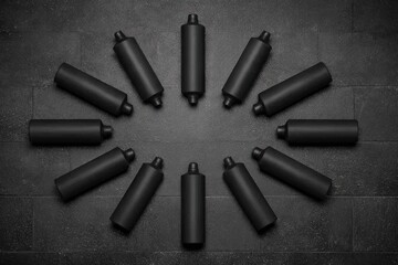 Naklejka premium Black cylindrical bottles arranged in a circle on a dark stone surface