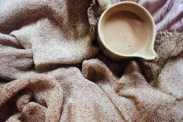 Cozy cocoa in a small cream pitcher nestled on a soft, textured throw blanket
