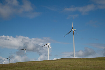 Wind turbines on top of a hill in a rural part of the country with blue skies and white clouds in the background