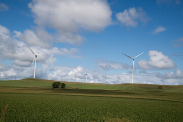 Wind turbines on top of a hill in a rural part of the country with blue skies and white clouds in the background