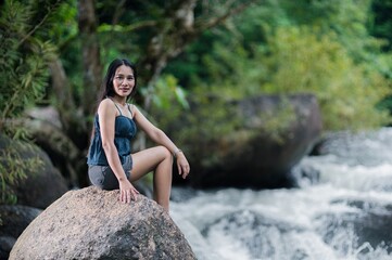 Fototapeta premium Woman Sitting on Rock by Stream in Lush Forest with Waterfalls