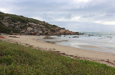 Obraz premium Peaceful beach with sand, gentle waves, vegetation and a rocky cliff at Rose Bay beach near Bowen in Queensland, Australia