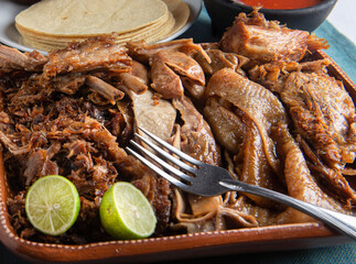 Traditional dish from central and southern Mexico called CARNITAS with a fork on top and lemon...