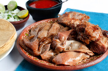 Traditional dish from central and southern Mexico called CARNITAS pork skin with hot or spicy red salsa on a mexican clay plate