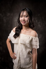 Young Asian woman standing and smiling in studio, wearing off-shoulder white blouse and layered...