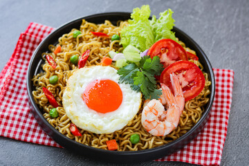 A plate of fried noodles with a sunny-side-up egg, prawns, fresh vegetables, and chili peppers.