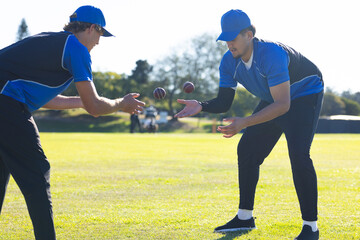 Two male athletes in blue jerseys practicing catching drill on grassy field with red balls