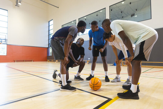 Diverse male teammates huddling around basketball on court with painted lines planning play - Powered by Adobe