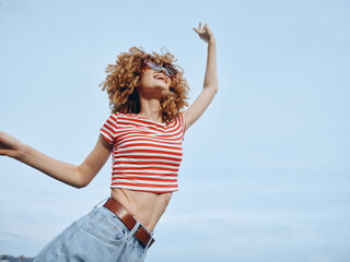Young dancer in a striped crop top and jeans pivots and leaps under a clear blue sky, embodying...