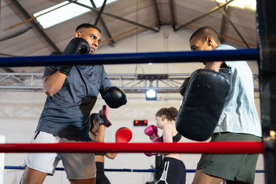 African american men sparring in boxing gloves in boxing ring inside gym with red-blue ropes