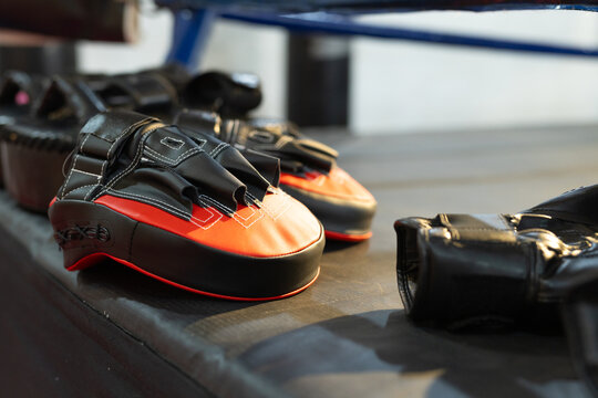 Black and red boxing pads are resting on platform under blue ring rope, showing stitching