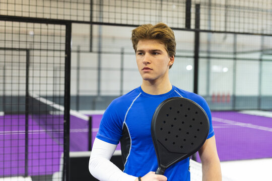 Male athlete gripping black racket while standing on purple padel court next to padel net