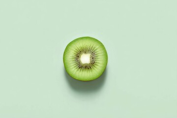 A perfectly centered cross-section of a kiwi fruit rests on a pale green background, casting a subtle shadow