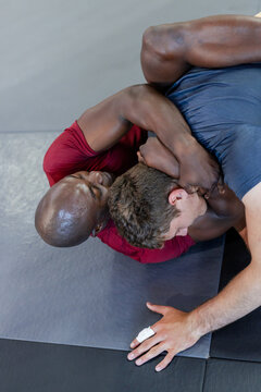 Diverse male training partners grappling on interlocking mats in gym with sports tape
