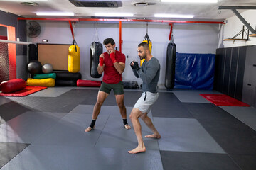 Diverse male training friends sparring on interlocking mats in combat gym with punching bags