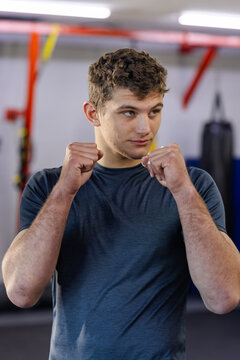 Male holding fists in boxing stance at gym in grey t-shirt with trx straps, punching bag