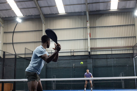 African american male athlete preparing backhand shot inside sports court with net, mesh fencing