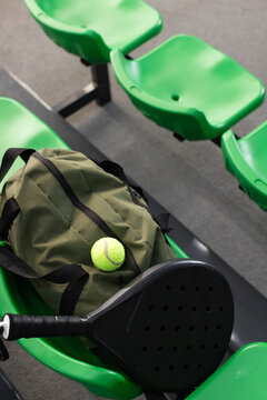 Olive duffel bag resting on seats at padel court with tennis ball, racket, copy space