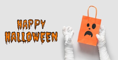 Banner with text HAPPY HALLOWEEN and mummy hands holding paper bag on white background