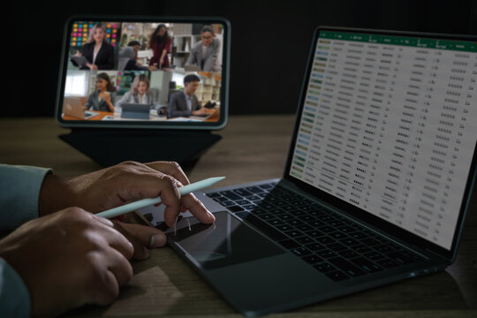 Close-up of remote worker using laptop for data analysis and tablet for online meeting, concept of webinar, digital learning, remote teamwork, and online presentation.