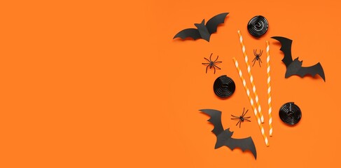 Halloween composition with bats, spiders and licorice candies on orange background with space for...