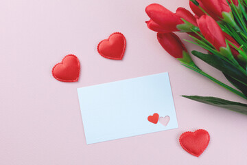 A romantic flat lay blank white card with two small heart, and red tulips on a soft pink...