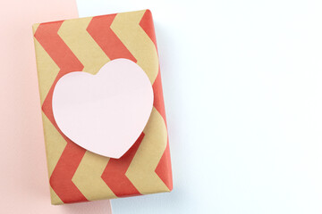 A neatly wrapped gift with red zigzag paper and a blank pink heart on a two-tone pink and white...
