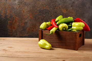 Box with different fresh peppers on wooden table
