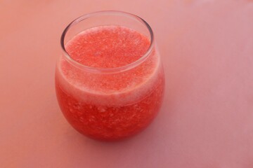 A glass of tamarillo (Solanum betaceum) juice with decorative slices of tamarillo on top seen from above isolated on a pink background, close-up view.