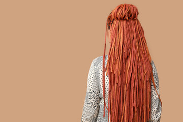 Young woman with dreadlocks on beige background, back view