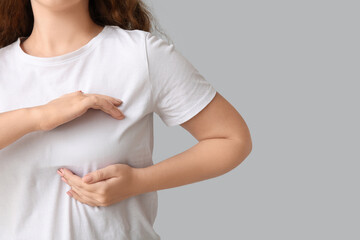 Young woman checking her breast on light background, closeup. Cancer awareness concept