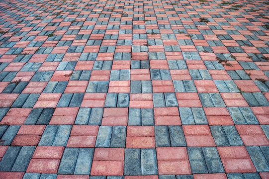 Paving stone surface featuring a pattern of red and gray bricks. The interlocking brick arrangement creates a textured ground cover suitable for walkways and driveways.