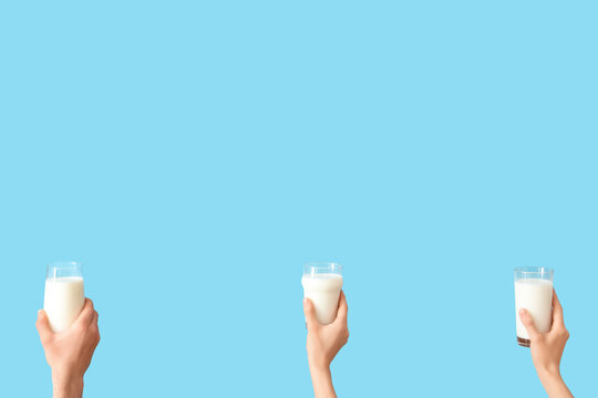 Hands with glasses of milk on blue background