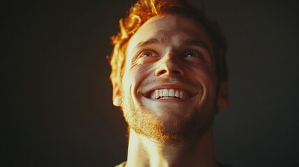 Man with red hair looking up and smiling with joy and hope in a close up portrait against a dark background