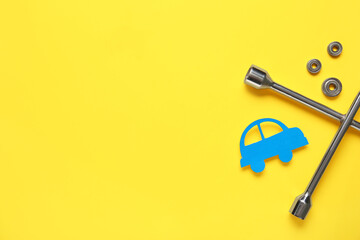 Cross wrench, nuts and toy car on yellow background. Mechanic concept