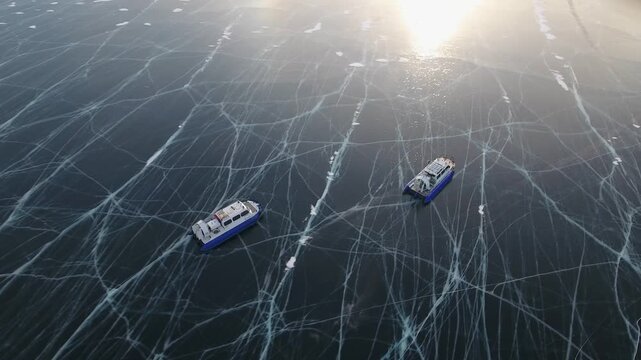 Aerial top down Two Hivus hovercrafts glide across endless winter ice of frozen Lake Baikal. Magnificent natural landscape, vast expanse UNESCO heritage site, amazing off-road adventure tourism Russia