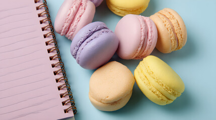 Fototapeta premium Pastel-colored macaroons and notebook arranged in overhead flatlay composition, sweet stationery concept --ar 16:9