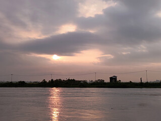 Beautiful sunrise over a calm river with cloudy sky and sunlight reflection on the water, creating...