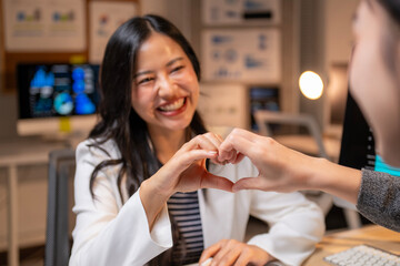 Two businesswomen smiling and making heart shape with hands in office