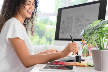 Female African-American graphic designer working with tablet at table in office