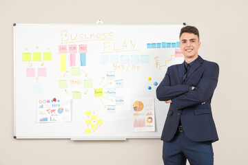 Fototapeta premium Young man near whiteboard with business plan on light wall