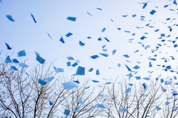 Blue confetti flutters against a pale sky, above leafless branches