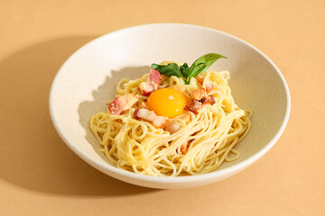 Bowl with tasty pasta carbonara on beige background, closeup