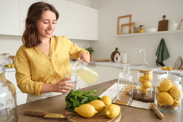 Young woman pouring lemonade into glass in kitchen