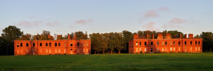 Abandoned red brick buildings in the evening sunlight with boarded windows and no roofs, surrounded...